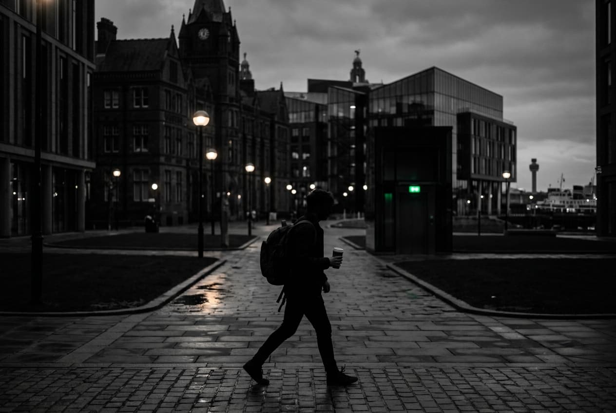 Student with a backpack crossing a Liverpool campus square at dusk